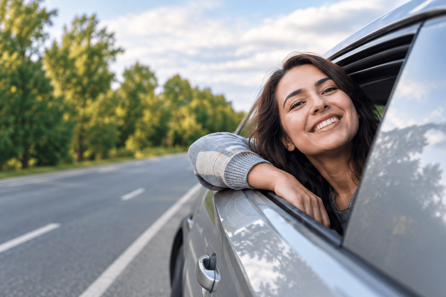 A smiling woman enjoying the journey in a silver car